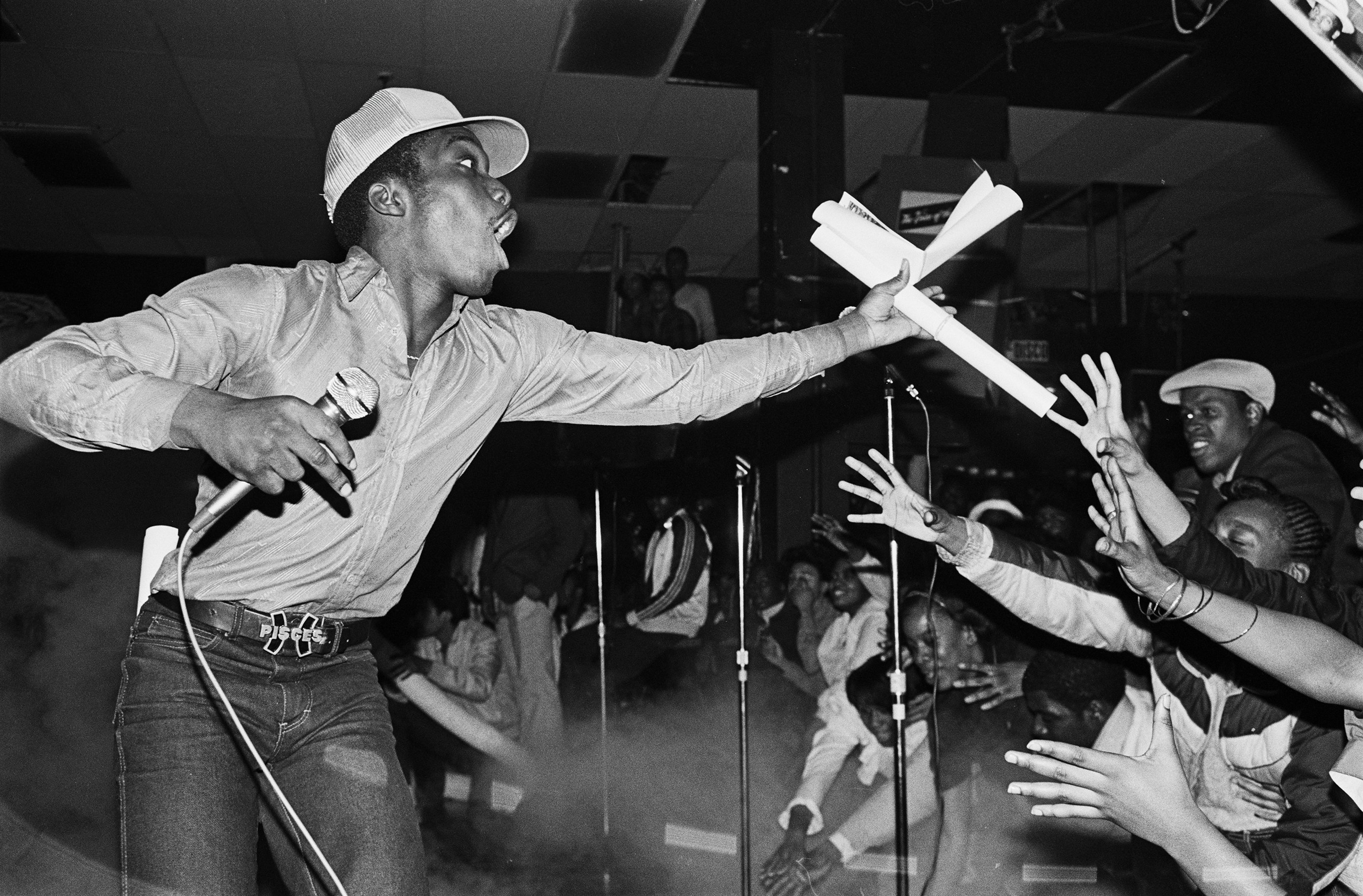 Almighty KG of the Cold Crush Brothers throwing out pictures to the crowds at Harlem World, 1981. Photo by Joe Conzo.